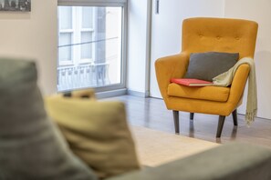 Uma sala de estar moderna com uma poltrona amarela, uma almofada cinza e um livro vermelho no apoio de braço.
