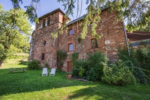 A stone building with a tower, surrounded by greenery and two white chairs in the foreground. - Ségonzac Cottage: Lake View, Private Terrace, Wi-Fi (Villecomtal)