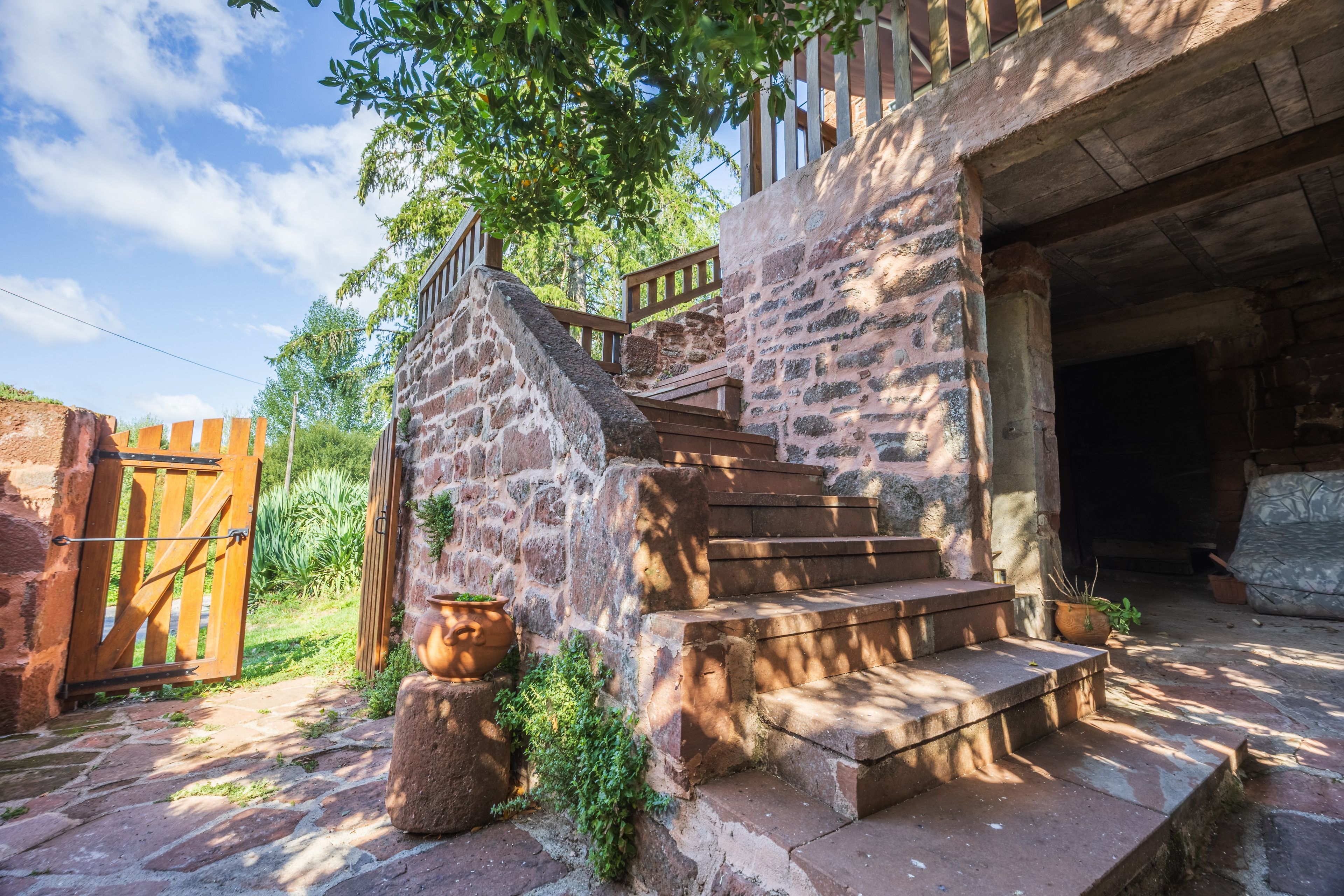 A rustic stone staircase leading to a wooden door, surrounded by greenery and a clear sky.