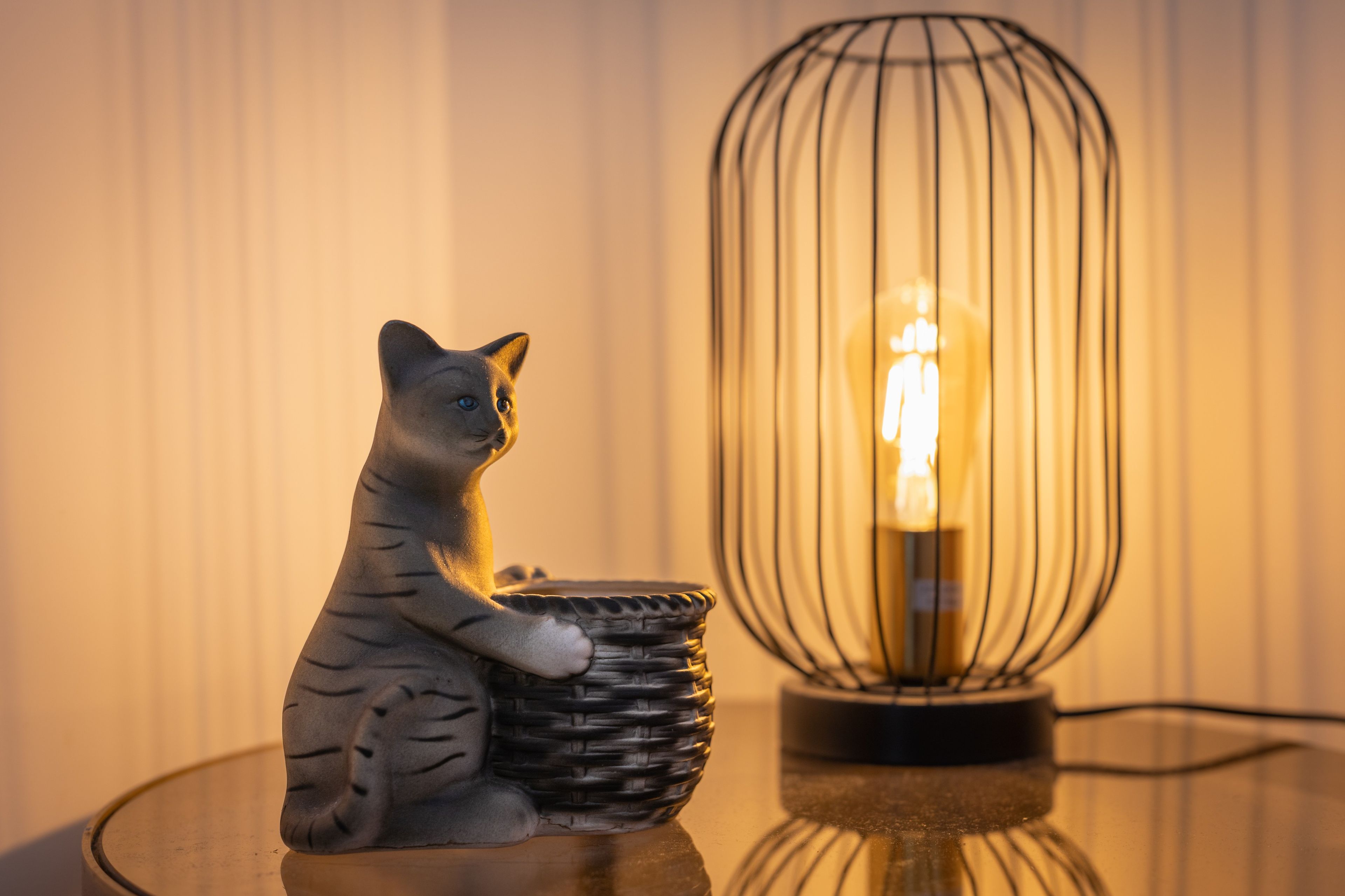 A cat figurine on a table with a lamp in the background.