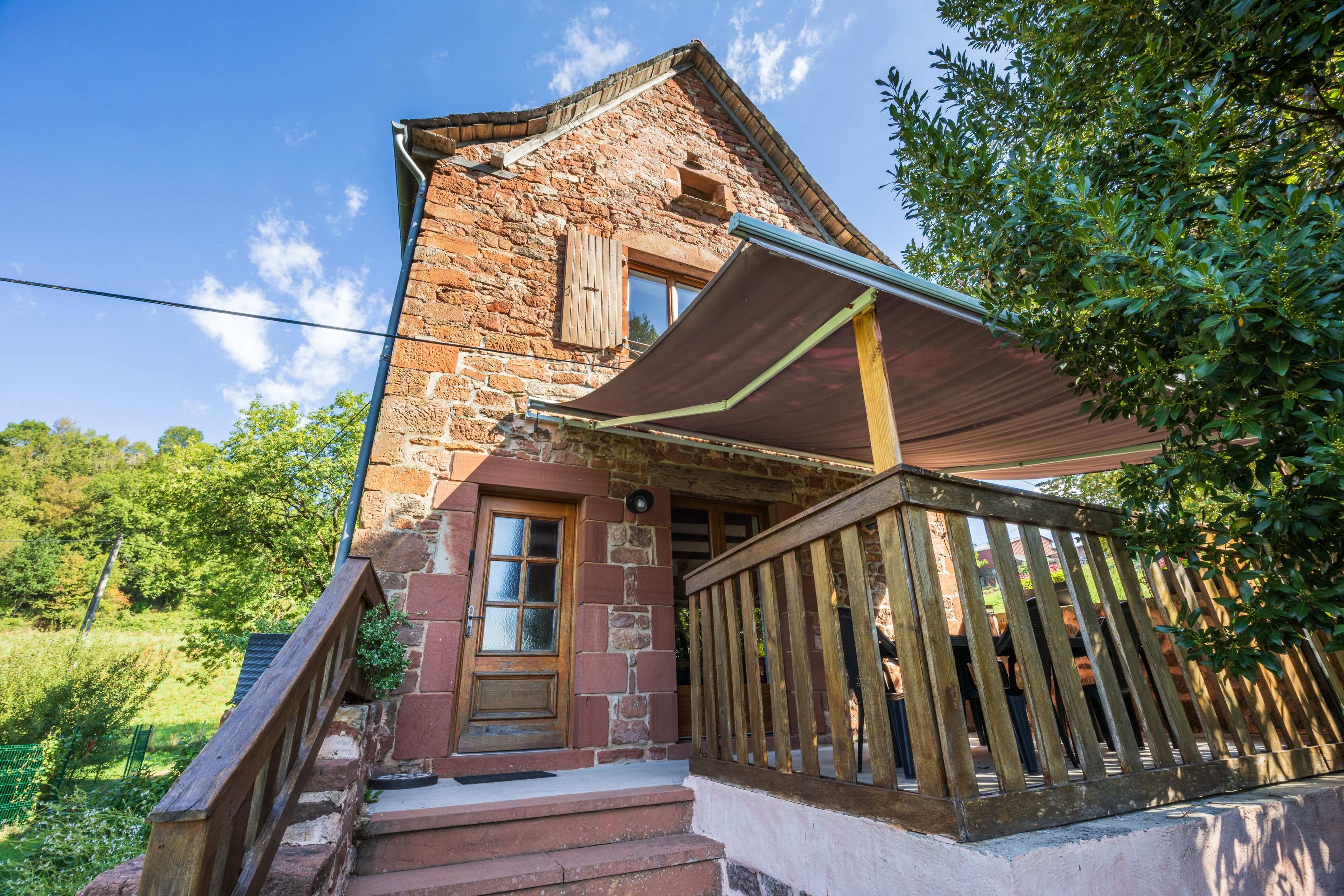 Ein Steinhaus mit einer Holztreppe, die zu einer Tür führt, einer Veranda mit Geländer und blauem Himmel im Hintergrund.