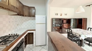 Una cucina con piano cottura a gas, frigorifero, pensili in legno e un'area pranzo con tavolo e sedie.