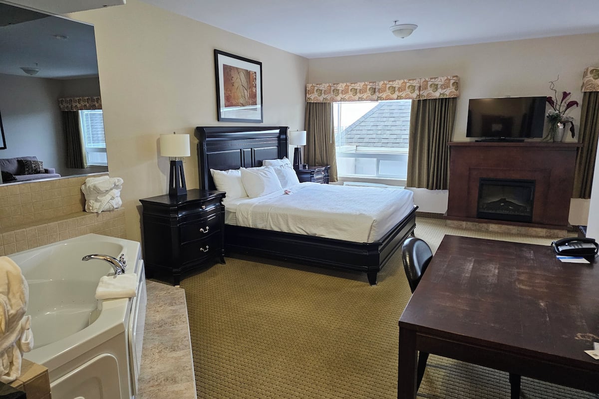 Quarto de hotel com cama, escrivaninha, lareira, televisão e banheiro com banheira e pia.