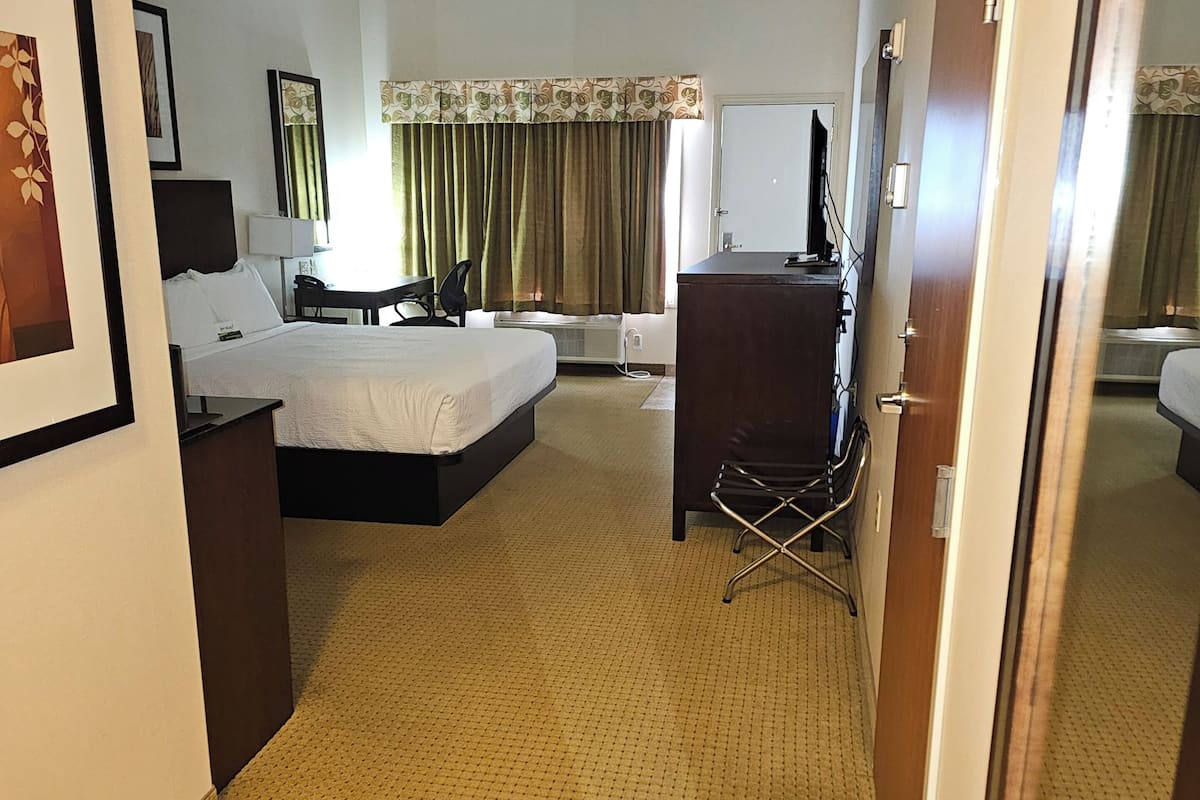 Quarto de hotel com cama, escrivaninha, cadeira e espelho.