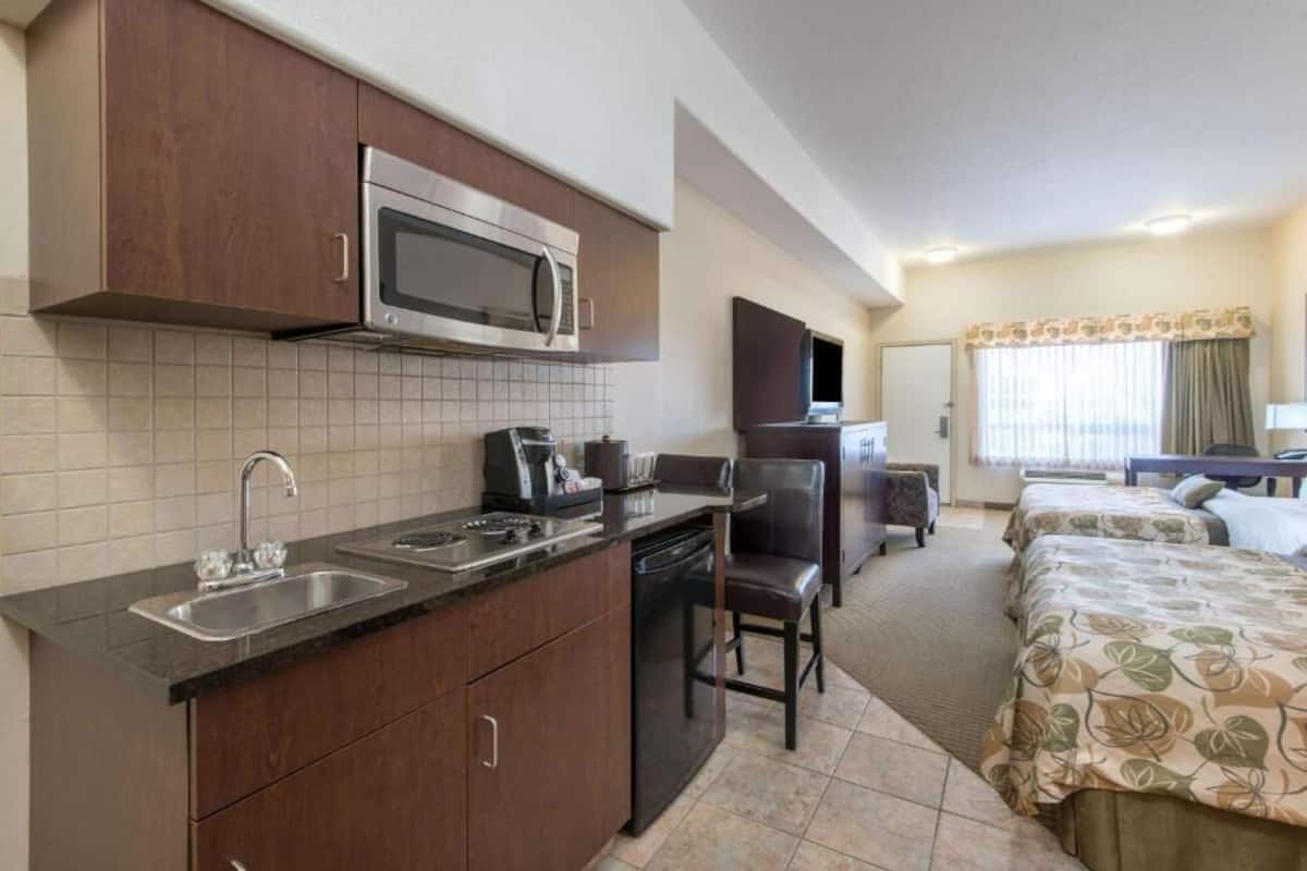Quarto de hotel pequeno com cozinha compacta, uma cama, televisão e janela com cortinas.