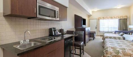 Habitación de hotel compacta con kitchenette, una cama, televisor y ventana con cortinas.