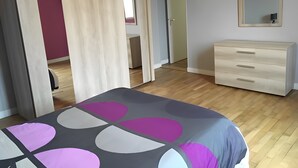 Une chambre à coucher comprenant un lit, une commode, un miroir et une porte donnant sur une autre pièce.