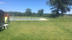 Un espace herbeux avec une piscine, une balançoire et un arbre.