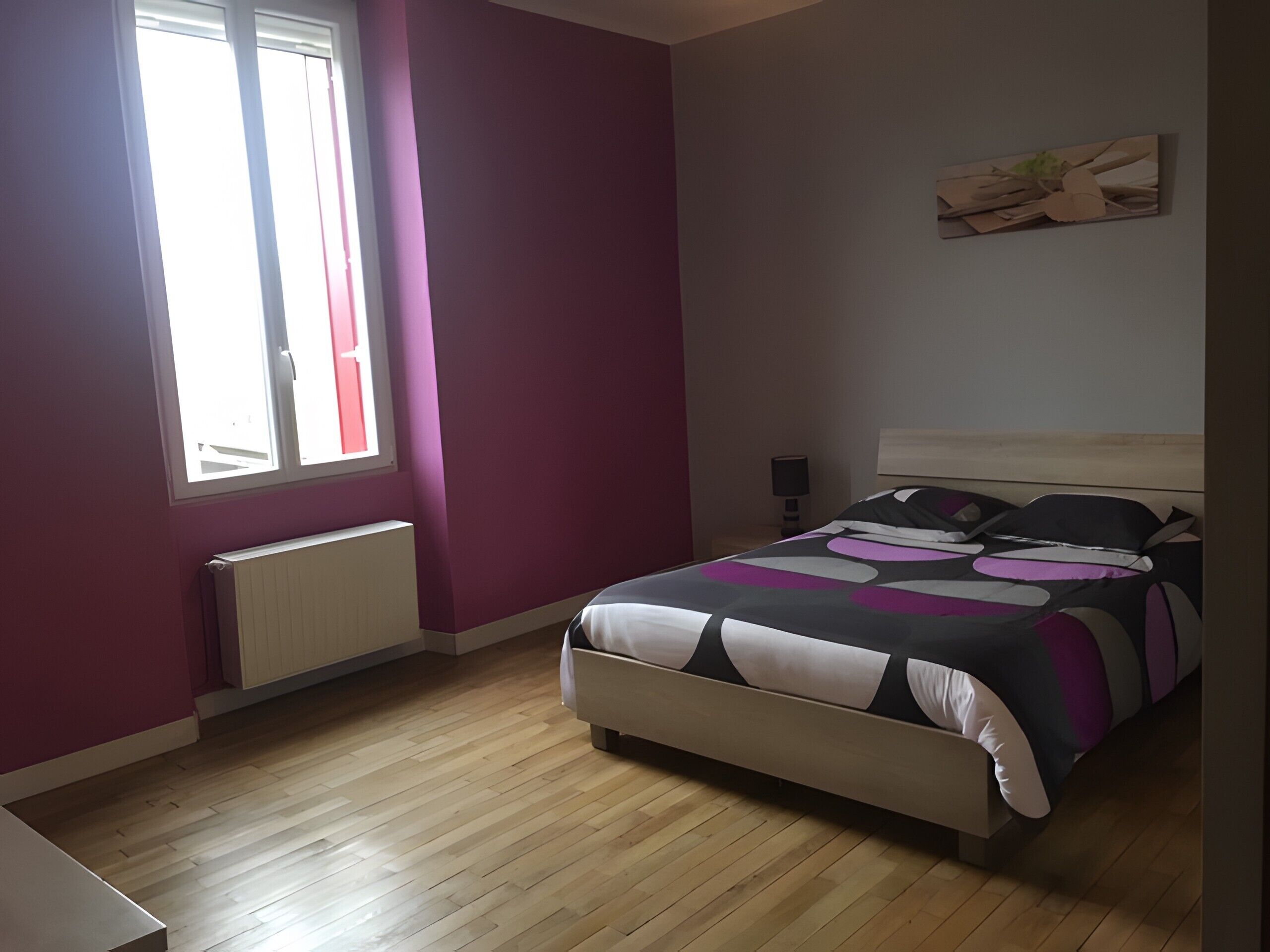 Ein Schlafzimmer mit Bett, Fenster, Heizkörper und einem Wandbild.