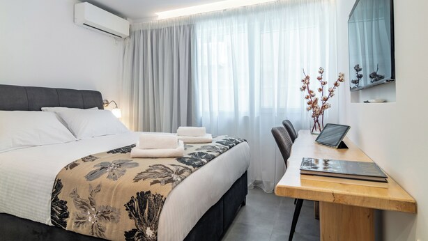 Una habitación de hotel moderna con una cama, un escritorio, una computadora portátil y una ventana con cortinas translúcidas.