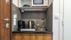 Una kitchenette compacta con microondas, cafetera, hervidor de agua y lavamanos.