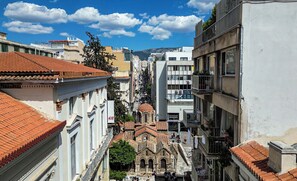 A narrow street with buildings, including a church with a dome, and a modern building with a sign. - Modern Studio in Syntagma - Walk to Acropolis (Athina)