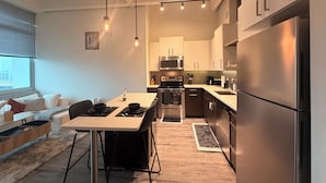 Una cocina moderna con electrodomésticos de acero inoxidable, un comedor con mesa y sillas, y una sala de estar con sofá y ventana.