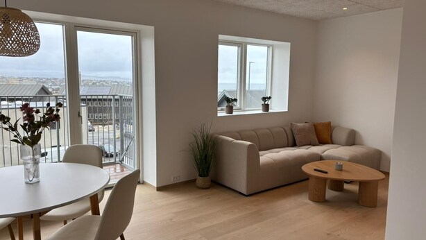 A modern living room with a sofa, a round table, and a balcony with a view. - Sea View Apartment with balcony 2BR (Argir)