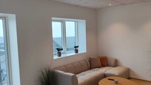 A modern living room with a sofa, a coffee table, and a window with potted plants. - Sea View Apartment with balcony 2BR (Argir)