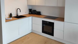 A modern kitchen with white cabinetry, a wooden countertop, a black sink, and a built-in oven. - Sea View Apartment with balcony 2BR (Argir)
