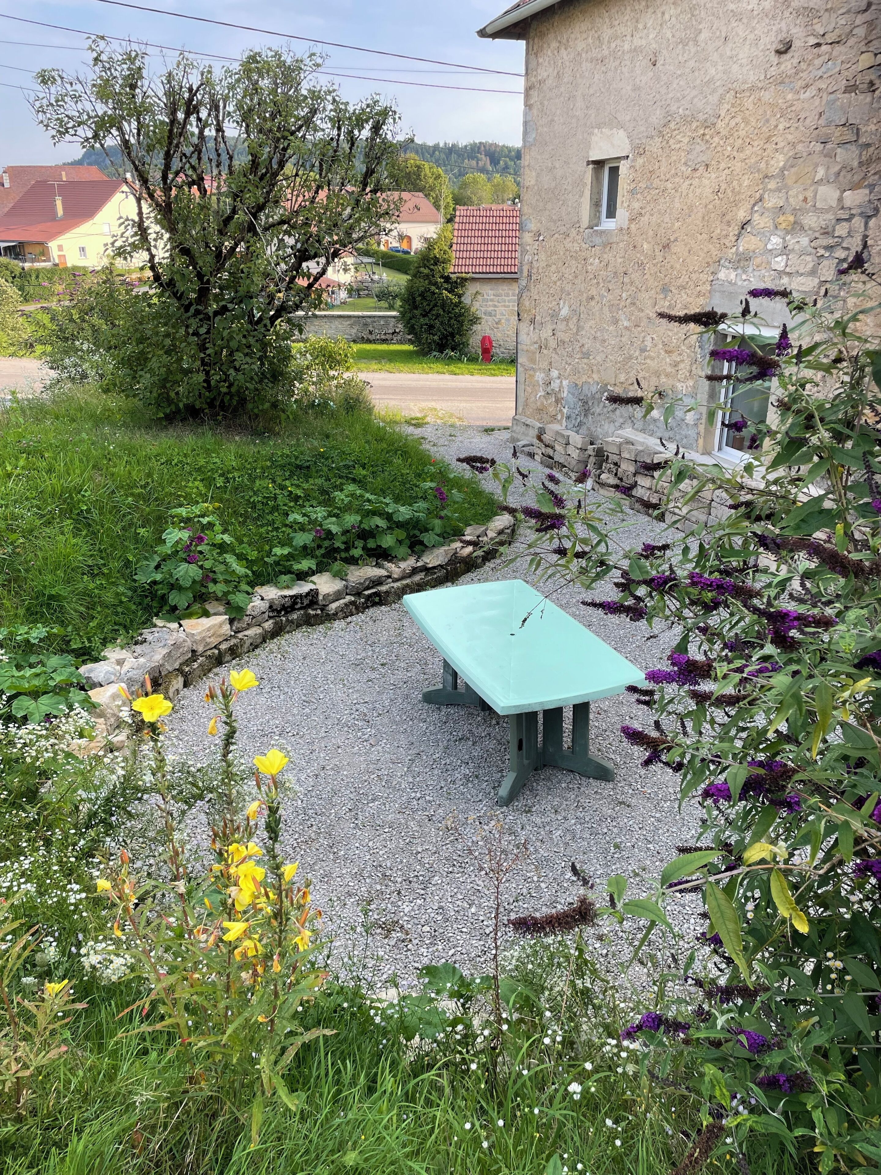 Un jardin avec un mur en pierre, un chemin de gravier et une table bleu clair.