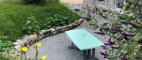 Un jardin avec un mur en pierre, un chemin de gravier et une table bleu clair.