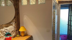 En rustik inredning med en trähylla, en lampa och utsikt genom en öppen dörr.