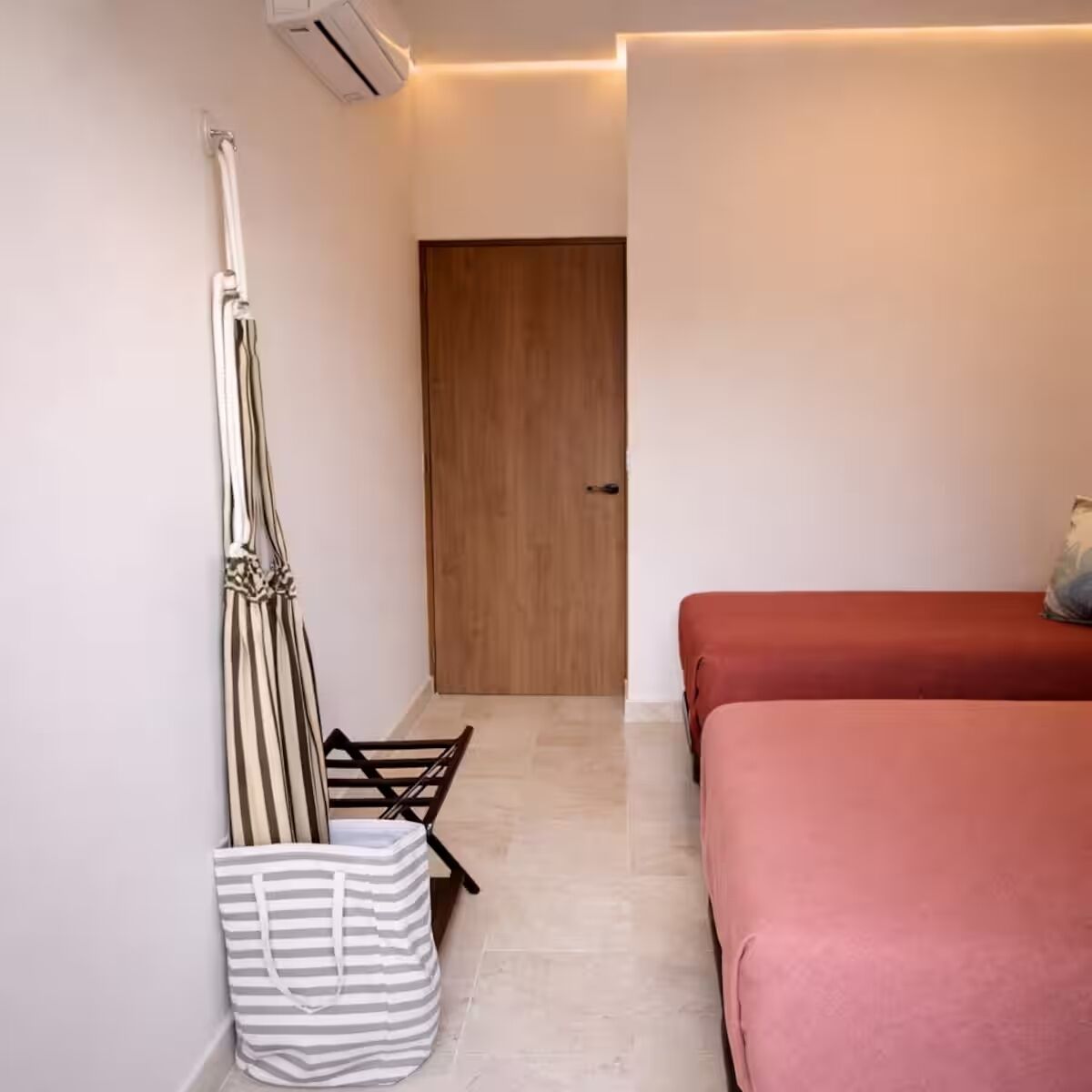 Une chambre avec un lit, une porte en bois, un sac à rayures et un canapé rouge.