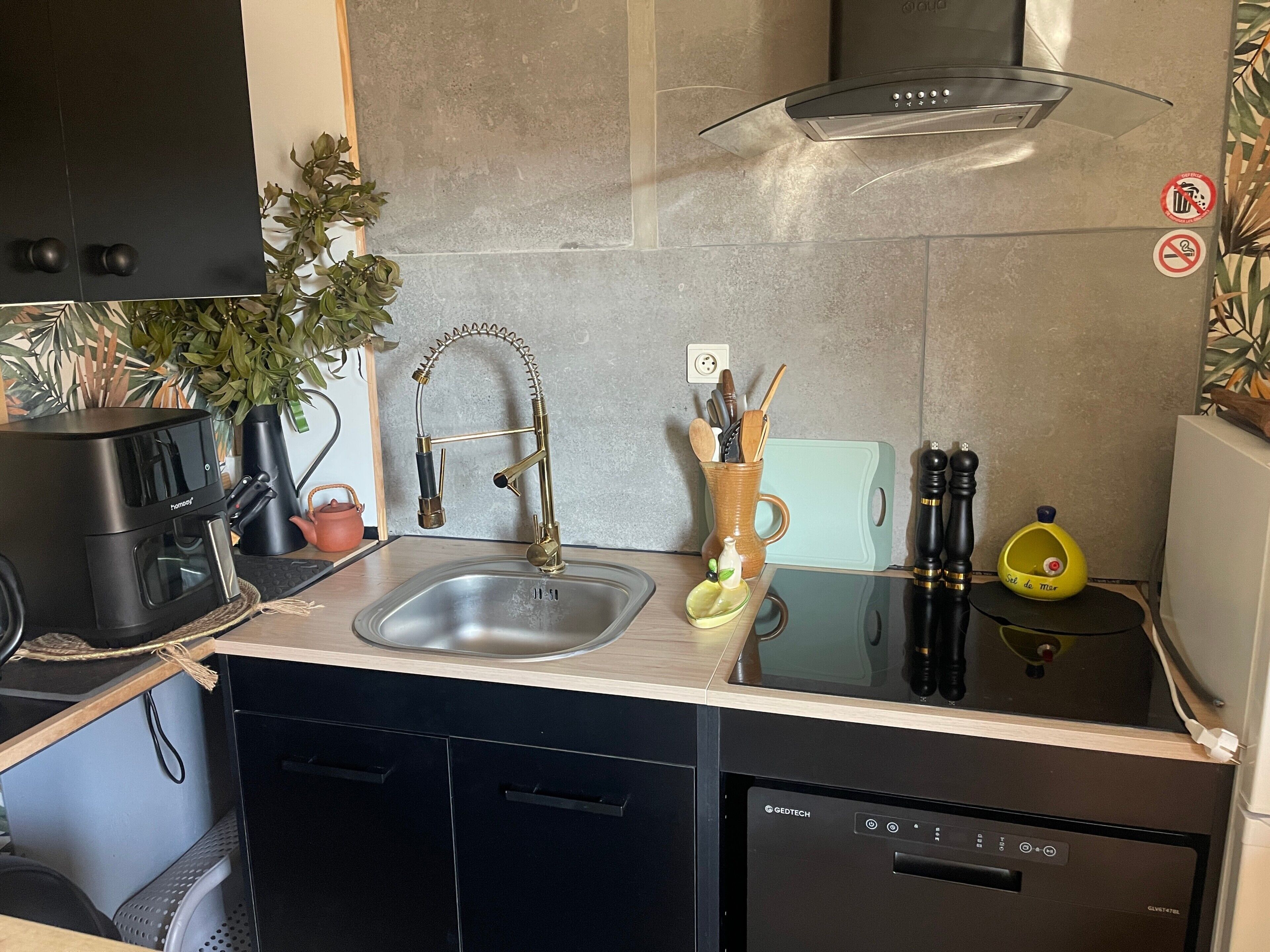Ett modernt kök med en inbyggd diskmaskin, en diskho i rostfritt stål och en köksfläkt.