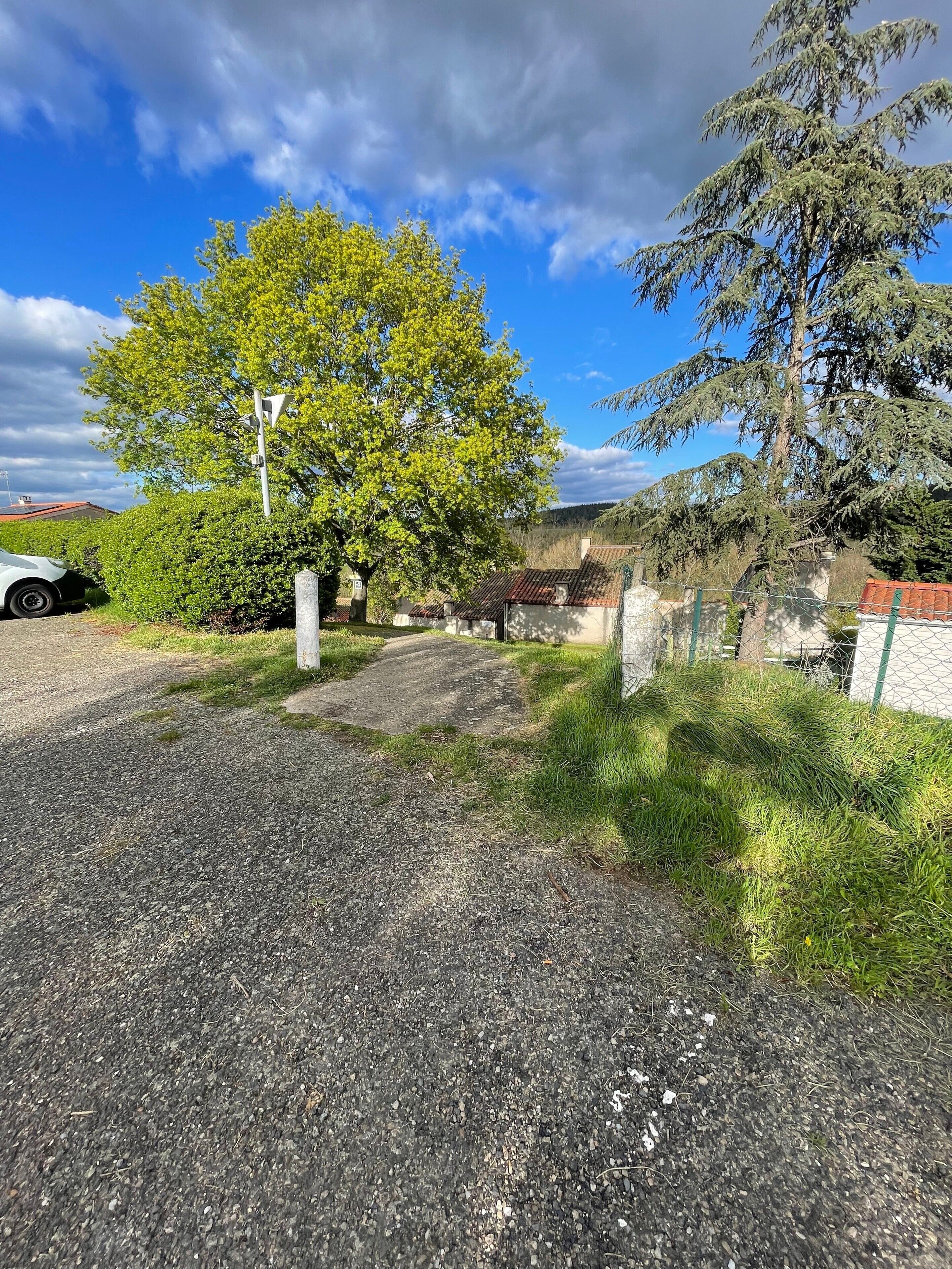 A gravel driveway leading to a building with a red roof, surrounded by greenery and a clear sky.