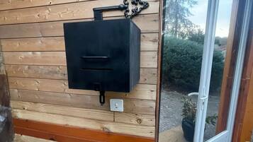 A wooden wall with a black outdoor grill, a white electrical outlet, and a sliding glass door leading to a garden.