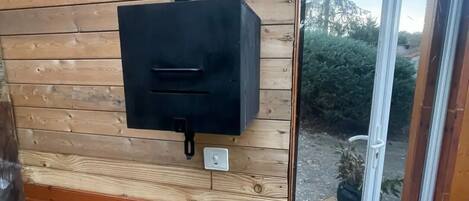 Eine Holzwand mit einem schwarzen Grill für den Außenbereich, einer weißen Steckdose und einer Glastür, die in einen Garten führt.