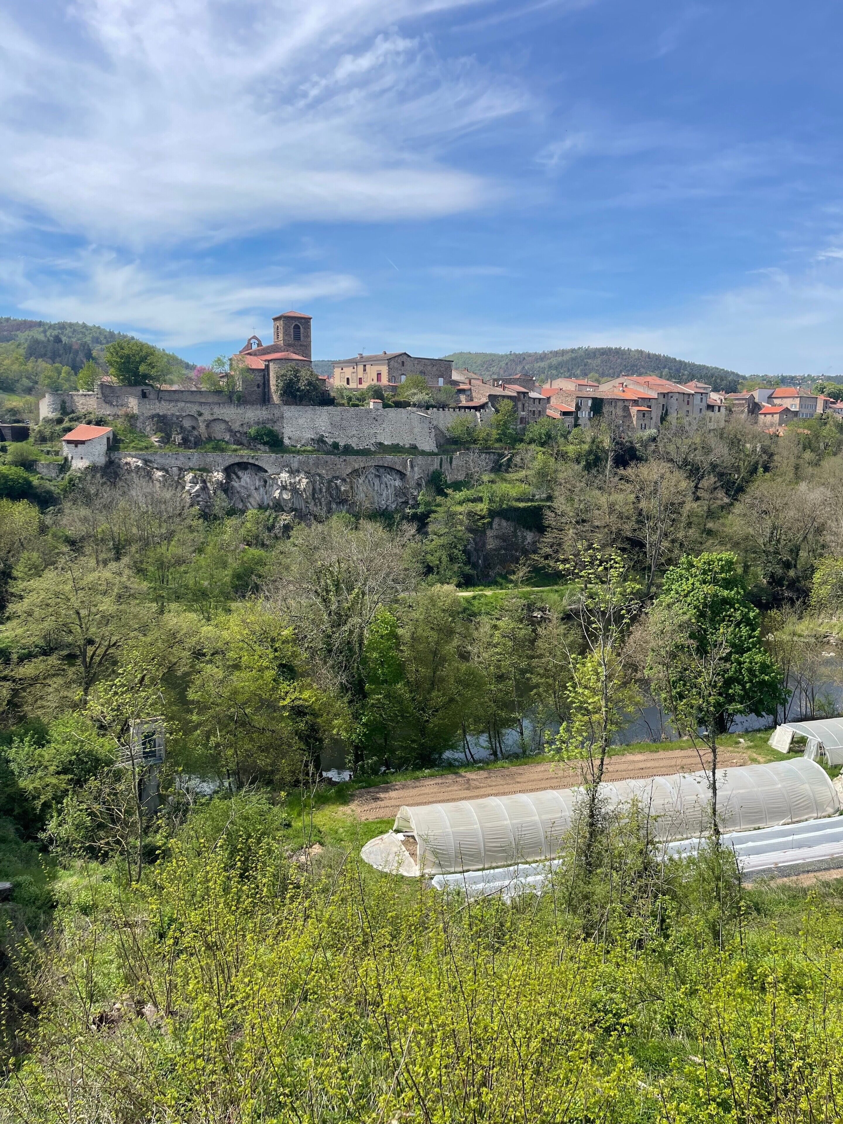 Un pueblo histórico con edificios de piedra, una torre destacada y abundante vegetación.