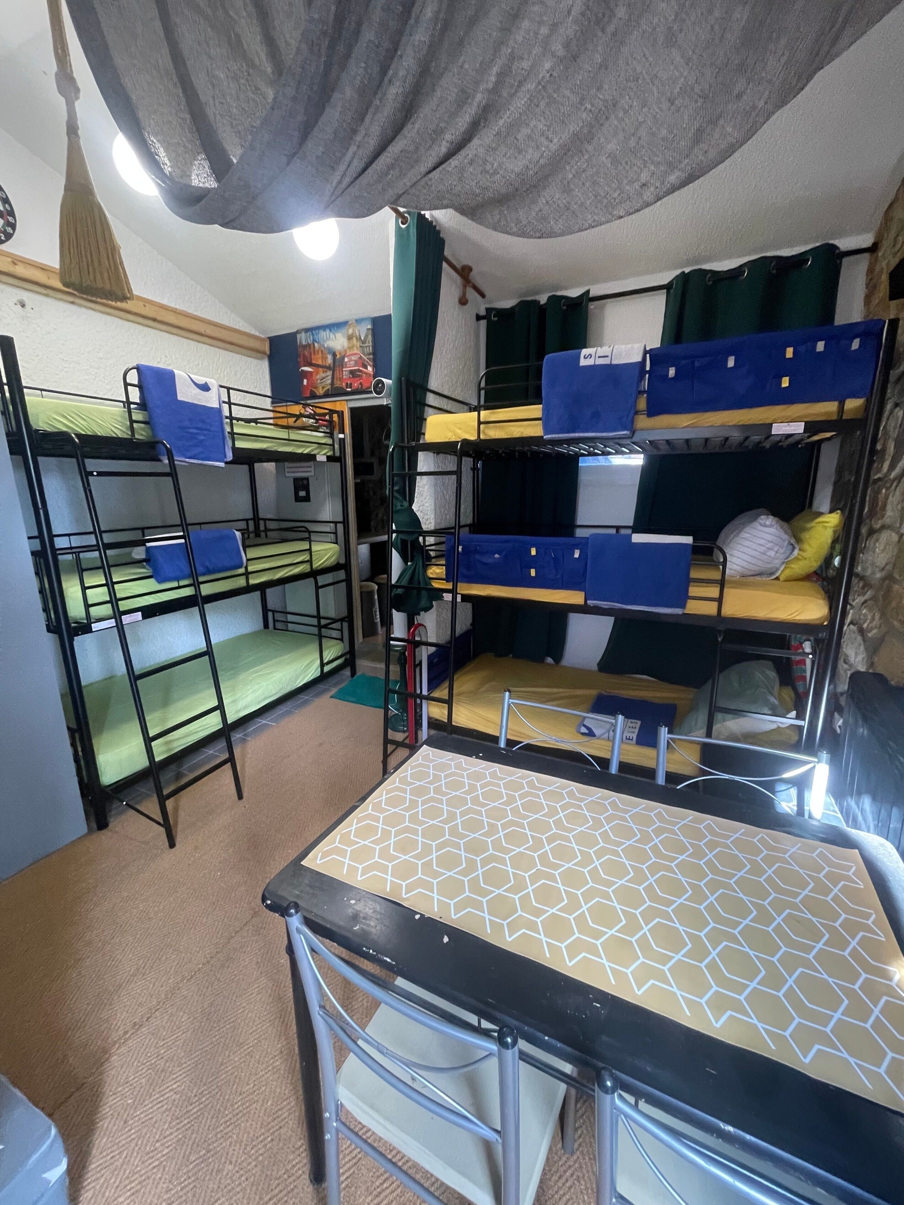 A dormitory room with bunk beds, a table, and a broom.