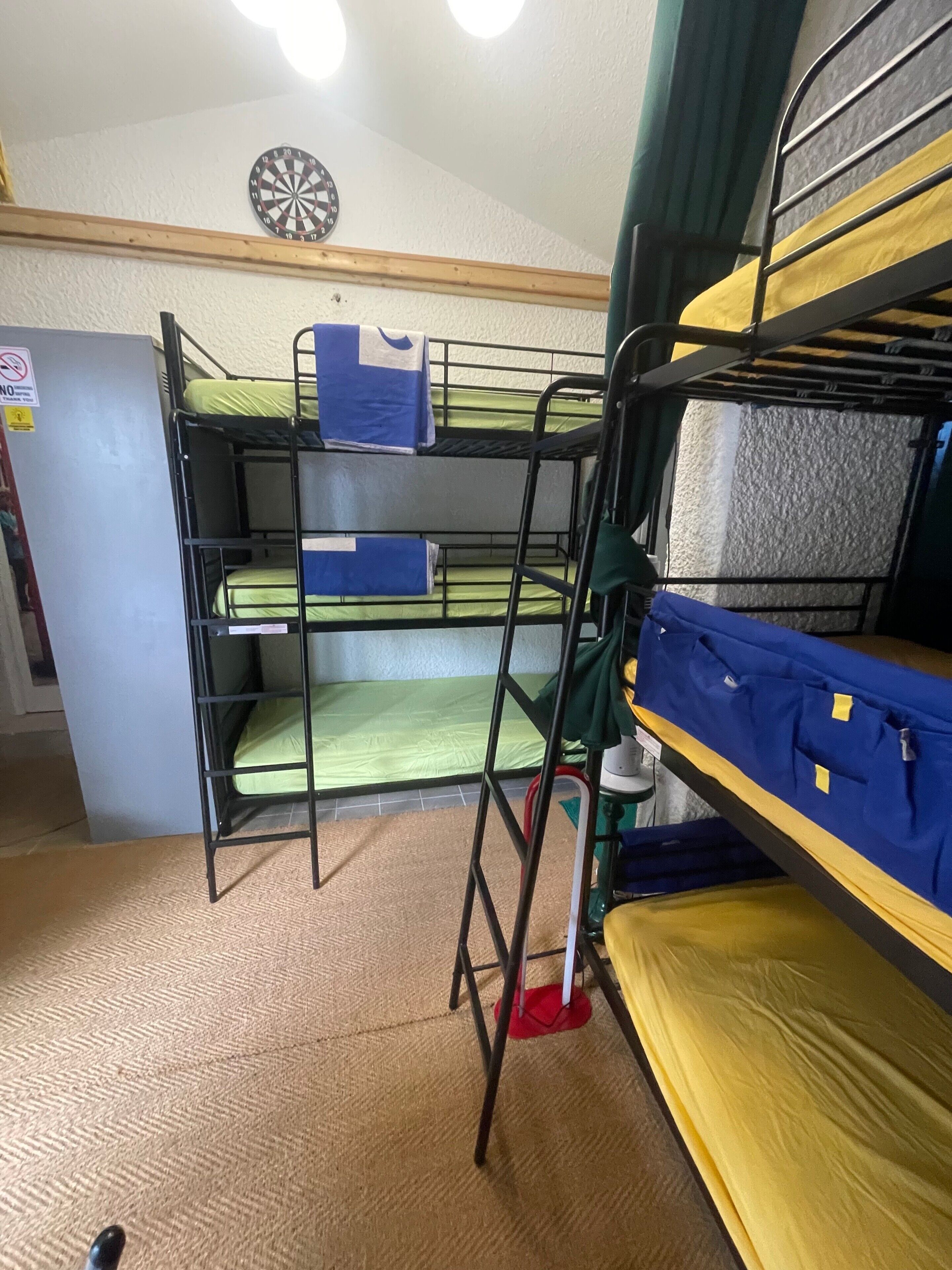 Habitación con literas, un dardo en la pared, un refrigerador pequeño y dispensador de agua.