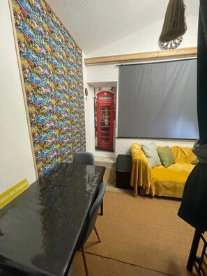 A room with a graffiti wall, a red telephone booth, a yellow sofa, and a black table.