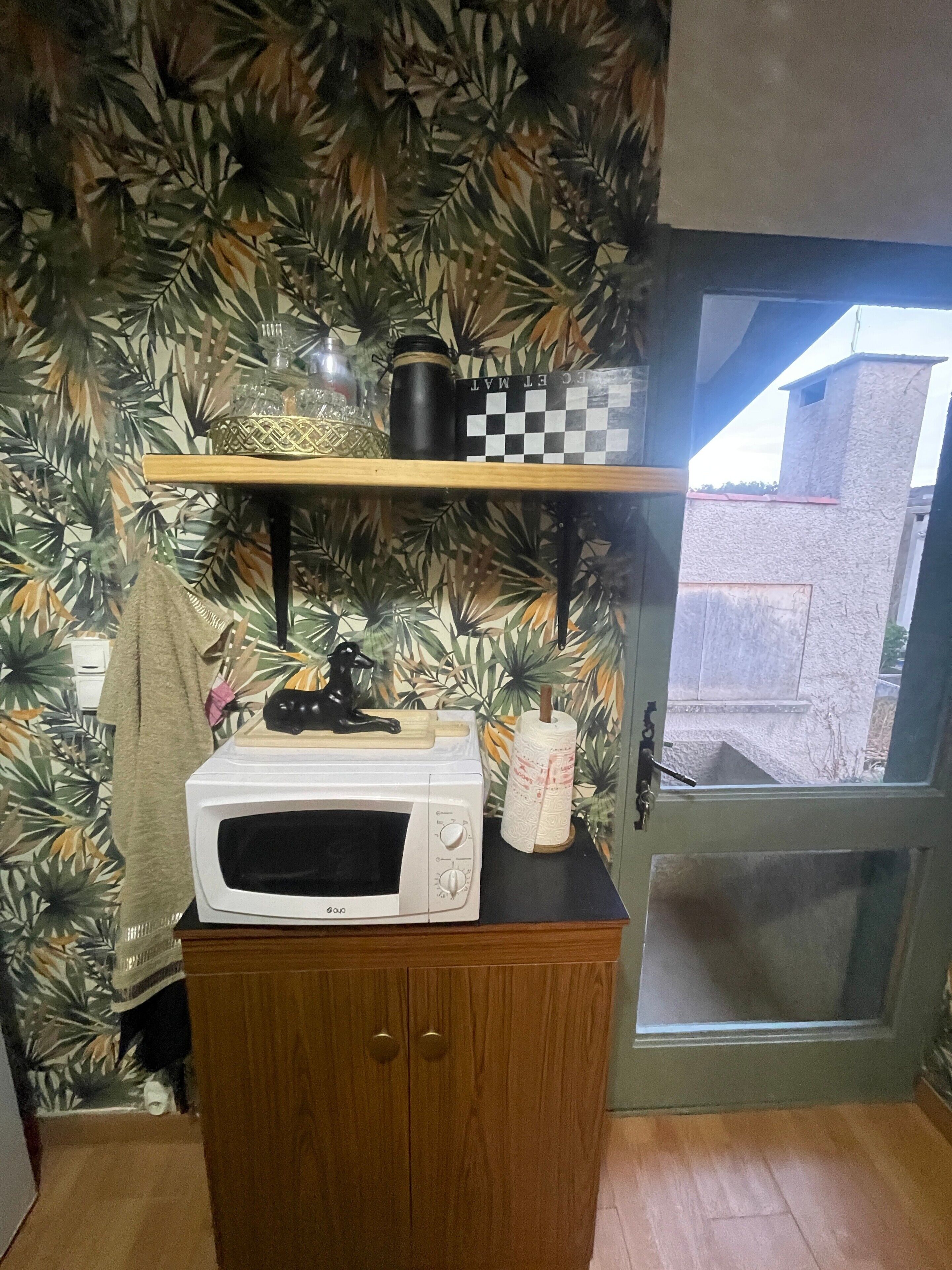 Una cocina con microondas, repisas con utensilios de cocina y una puerta con vista.