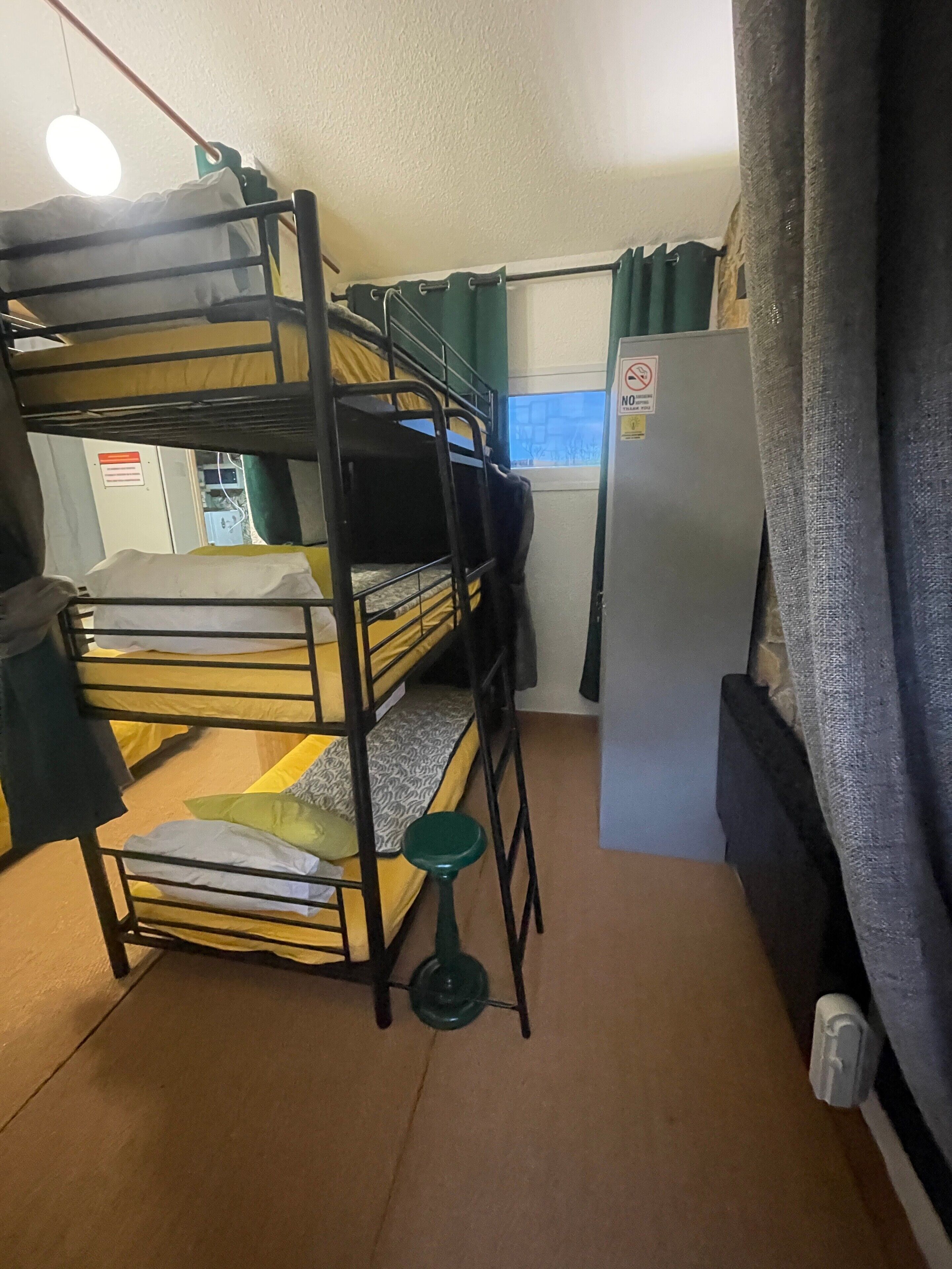 A bunk bed room with a window, a refrigerator, and a small stool.