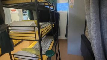 Kerrossängyllä varustettu huone, jossa on ikkuna, jääkaappi ja pieni jakkara.
