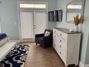 A room with a bed, a dresser, a chair, a TV, and a window with blinds.
