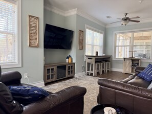 A living room with a television, a sofa, a coffee table, and a small kitchen area with stools.