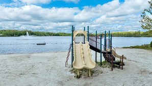 Une aire de jeux avec un toboggan et des structures d’escalade, située près d’un lac.