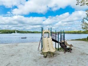 A playground with a slide and climbing structures near a lake. - Sleeps 14 - Hot Tub ·Fire Pit - Pool/Beach Access (Pocono Summit)