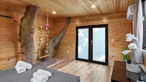 A wooden cabin room with a bed, a hanging flower arrangement, and a sliding glass door.