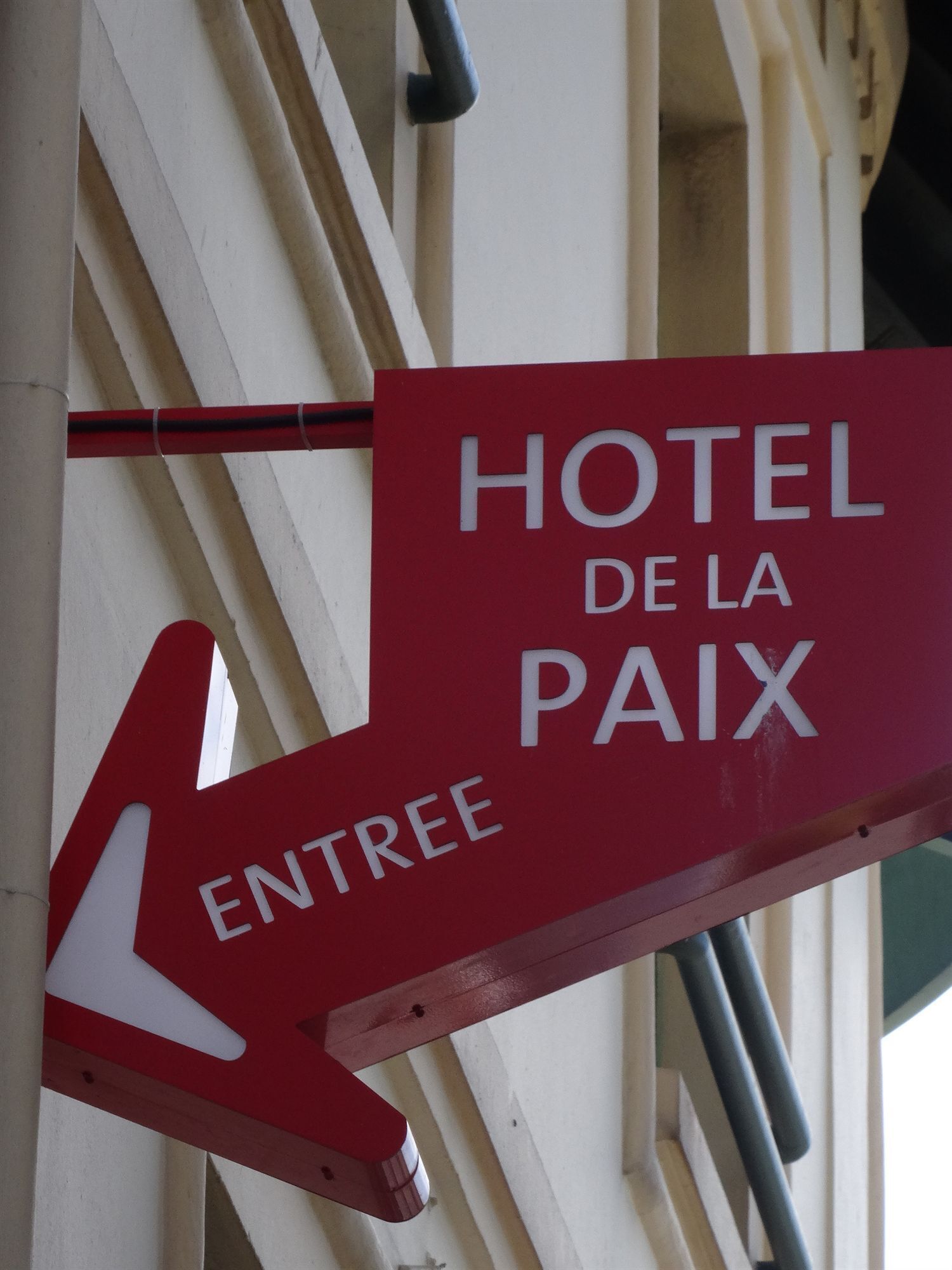 A red sign with white lettering indicating 'HOTEL DE LA PAIX' and an arrow pointing left for 'ENTREE'.