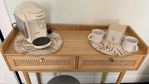 A wooden desk with a coffee maker, two white cups, and a small table with a leaf-patterned coaster.