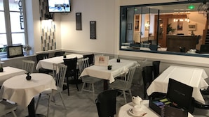 A hotel dining area with tables, chairs, a television, menu boards, and a mirror reflecting the interior.
