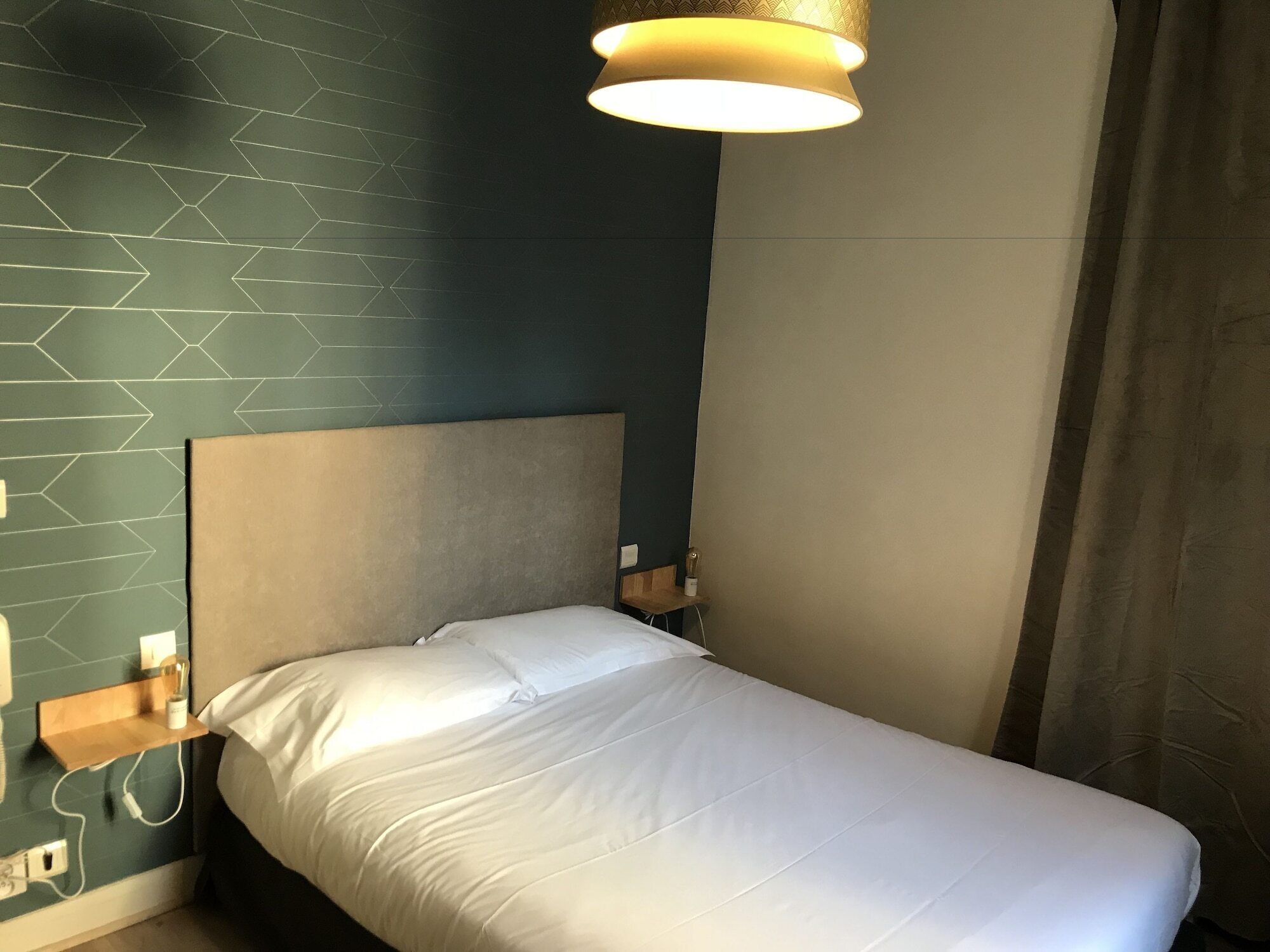Ein Einzelbett mit Kopfteil, ein Nachttisch, eine Lampe und eine Wand mit geometrischem Muster.