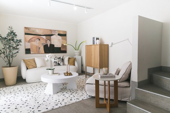A modern living room with a white sofa, a round coffee table, a wooden cabinet, a potted plant, and a painting on the wall.