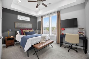 Un dormitorio con cama, mesita de noche, escritorio, silla, televisor y ventana con cortinas.