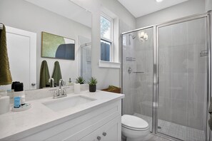 Un baño moderno con un espejo grande, un lavamanos, un inodoro y una ducha con mampara de vidrio.