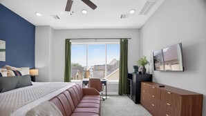 A bedroom with a bed, a brown leather sofa, a desk, a cabinet, and a TV on the wall. - Urban EaDo Retreat - 3BR Townhome w/ Deck (Houston)