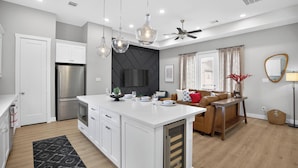 A modern kitchen with white cabinetry, a central island, and a dining area with a brown sofa and a TV. - Urban EaDo Retreat - 3BR Townhome w/ Deck (Houston)