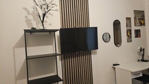 Une pièce avec un téléviseur fixé au mur, un panneau en lamelles de bois, un bureau blanc et un miroir.